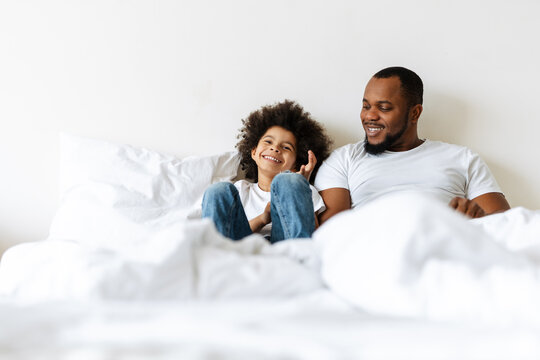 Black father and son laughing while lying in bed at home