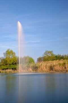 Big water fountain in a lake with a blue sky in the background in Bussy Saint Georges France