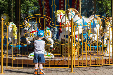 The child looks at old French carousel in a holiday park. Horses on a traditional fairground...