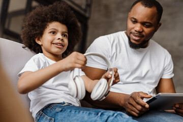 Black father and son using tablet computer and headphones at home