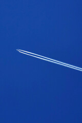the plane flies across the blue clear sky, leaving a trail