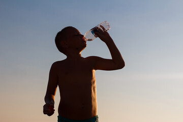 short-haired boy drinks water from a bottle in a counter light. silhouette