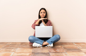 Young mixed race woman with a laptop sitting on the floor making time out gesture