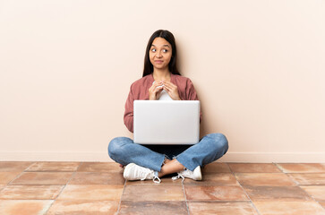 Young mixed race woman with a laptop sitting on the floor scheming something