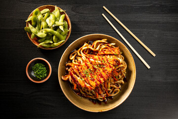 Closeup of Japanese noodles and crispy chicken, viewed from above on dark background.