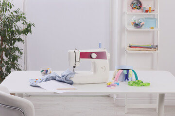 Modern sewing machine, fabric and accessories on table indoors