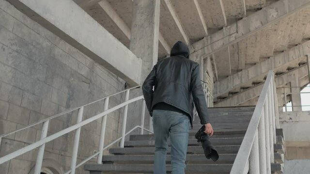 A private detective or spy with a camera climbs the steps of an abandoned stadium.