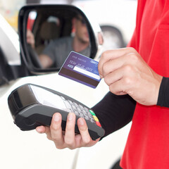 Gas station staff swipe credit card via payment terminal after giving a price quote to the customer sitting in the car.