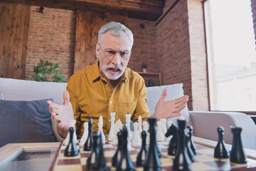 Photo of angry impressed mature man play chess wear spectacles yellow shirt at home alone