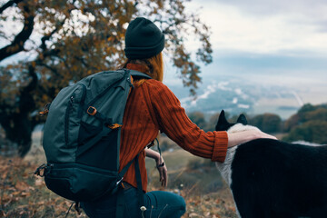 woman with backpack in nature plays with dog in mountain landscape