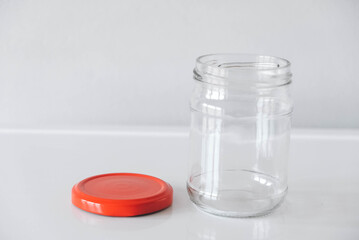 Empty glass jar with red cover on white table background. Copy, empty space for text