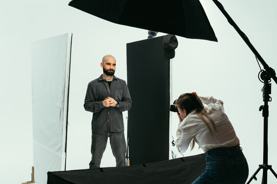Woman photographer makes a photo shoot for a handsome bearded man in a photo studio on a white background. Backstage photo photography process.