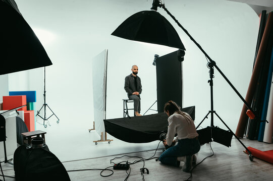 Woman photographer and bearded man model working in a photo studio on a white background with flashes. Backstage photo process photo shoot.