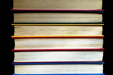 The covers of colorful books in a stack on a dark background. Rainbow stack of books
