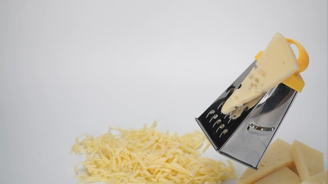 cheese is shredded on a grater. preparation of dishes with the use of cheese parts.  culinary work. kitchen grater on a white background. Stop motion. 