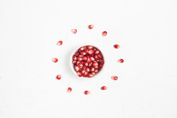 Grains of red ripe pomegranate in a ceramic plate on a white textured background top view