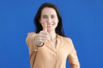 Young woman showing thumb up on blue background closeup