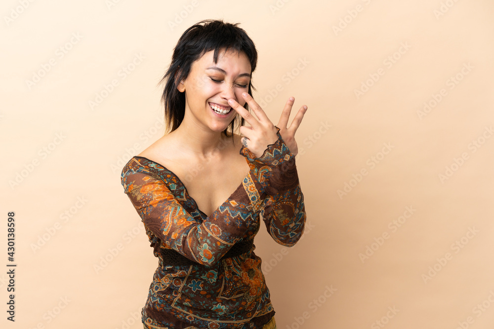 Wall mural indian woman isolated on beige background smiling and showing victory sign