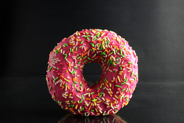 Berliner Donat in pink glaze with colored topping on a black background with a place for text and a copyspace of the delicious food cooking tomorrow's dessert
