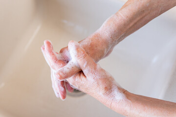 Fototapeta premium Elderly woman washing her hands with soap in a kitchen sink. Concept of personal hygiene for ncov corona virus (covid-19) infection prevention or general healthcare. Close-up, top view.