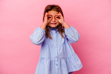 Little caucasian girl isolated on pink background  showing okay sign over eyes