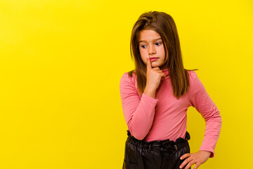 Little caucasian girl isolated on yellow background looking sideways with doubtful and skeptical...