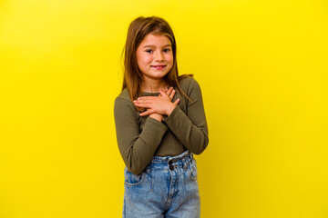 Little caucasian girl isolated on yellow background laughing keeping hands on heart, concept of...