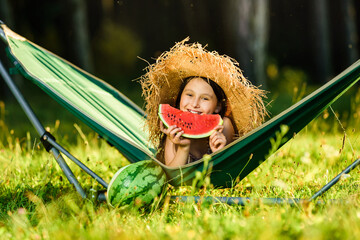 Summer weekend at sunset near the forest. Little happy lying resting in a hammock. Eats a slice of watermelon. Sunny summer vacation.