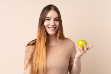 Young caucasian woman isolated on beige background with an apple and happy
