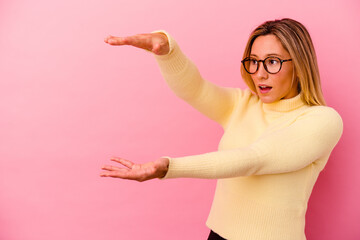 Young mixed race woman isolated on pink background shocked and amazed holding a copy space between hands.