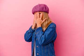 Young mixed race woman isolated on pink background blink through fingers frightened and nervous.