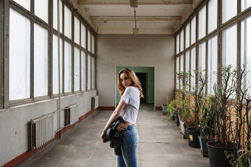 pretty girl stands in centre of old room with windows, radiators and houseplants