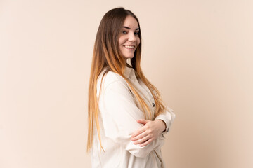 Young caucasian woman isolated on beige background looking to the side and smiling
