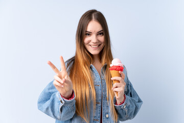Young woman with a cornet ice cream isolated on blue background smiling and showing victory sign