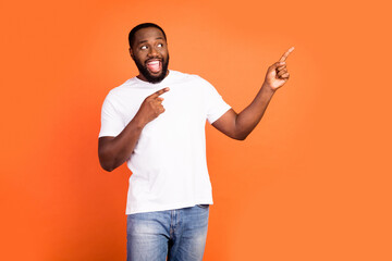 Portrait of attractive cheerful guy demonstrating copy empty space ad look idea isolated over bright orange color background