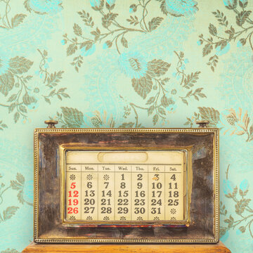 Ancient office table calendar in front of vintage blue wallpaper with floral pattern