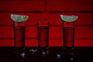 Shot of tequila with salt and lemon and reflection on bright table. Bar with colored lights. The celebration concept. A red night in the bar. Close up with soft focus.
