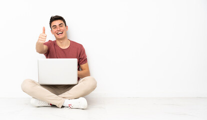 Teenager man sitting on the flor with his laptop with thumbs up because something good has happened
