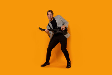 stylish and cool guy in a suit and with a game guitar on a yellow background,