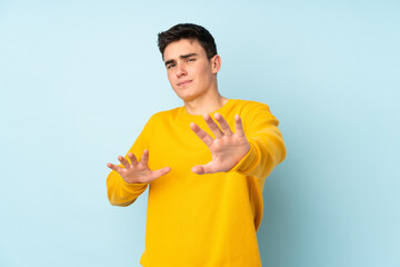 Teenager caucasian handsome man isolated on purple background nervous stretching hands to the front