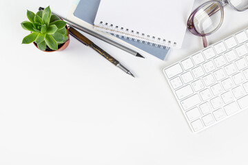 Flat lay, office table top view. Workspace with blank notebook, keyboard, stationery, pencil, succulent in a pot on a white background.