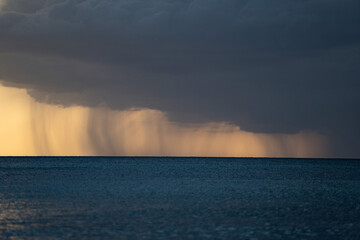 Heavy rain, stormy clouds and storm over seascape during dramatic sunset 