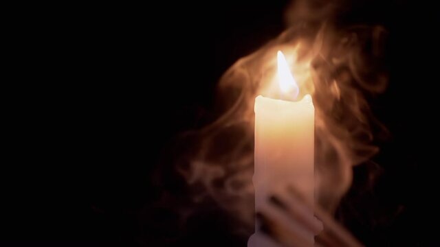 Burning White Paraffin Candle with a Bright Flame in a Smoky Room. A wax candle burns in a cloud of smoke on black background. Smoky room. Concept of memory, ritual, celebration. Slow motion. 180 fps.