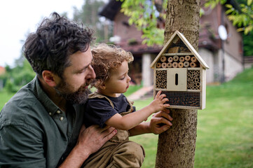Small girl with father holding bug and insect hotel in garden, sustainable lifestyle. © Halfpoint