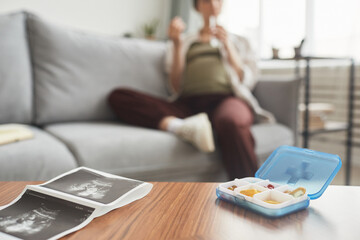 Close-up of tale with ultrasound image with box with vitamins on it and pregnant woman sitting in the background