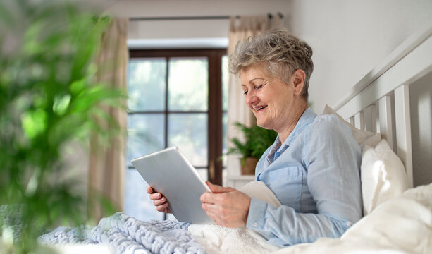 Happy Senior Woman Using Tablet In Bed At Home.