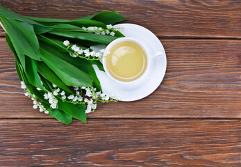 Cup of green tea with lily of the valley or may bells flowers on a wooden background. Copy space. Top view.