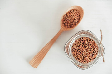 Buckwheat kernels in a glass jar and spoon on white background. Top view. Copy, empty space for text
