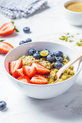 Matcha oatmeal bowl with berries and maple syrup on white marble background. Healthy breakfast, vegan food, detox recipe.