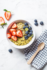 Matcha oatmeal bowl with strawberries, blueberries and hemp seeds on white marble background, top view. Healthy breakfast, vegan food, detox recipe.